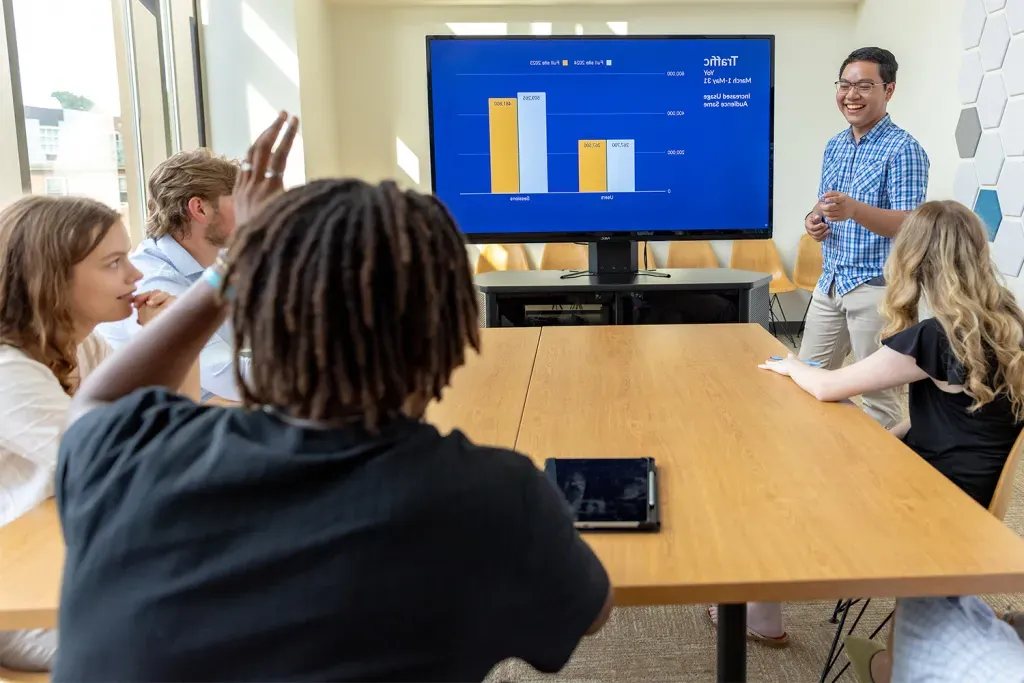 One UNE student presents to a groups of business students and one raises a hand to ask a question